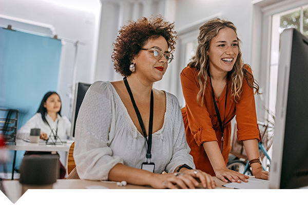 Two women talking and looking at a monitor screen, one of them is typing