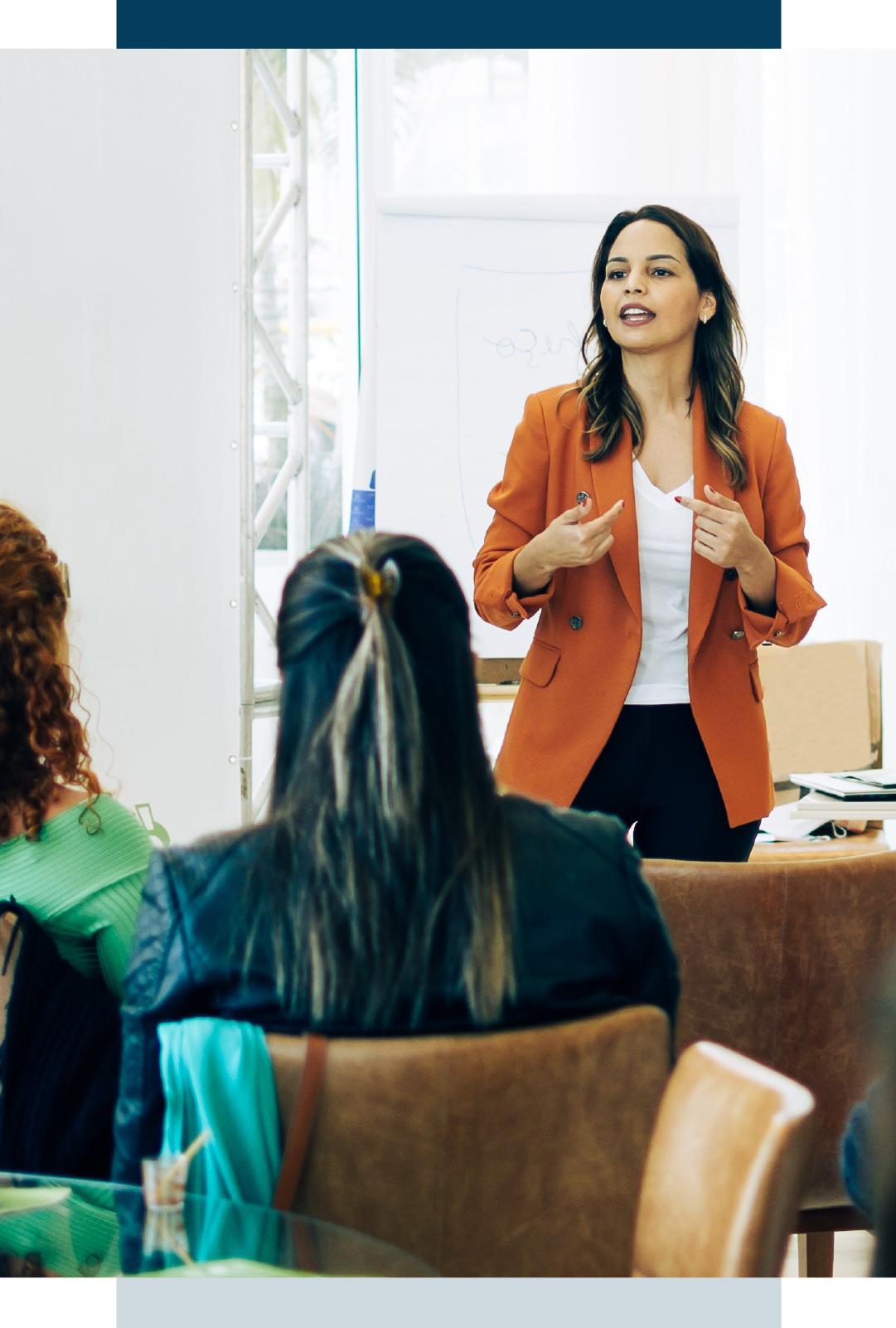 Woman in orange blazer talking to classroom